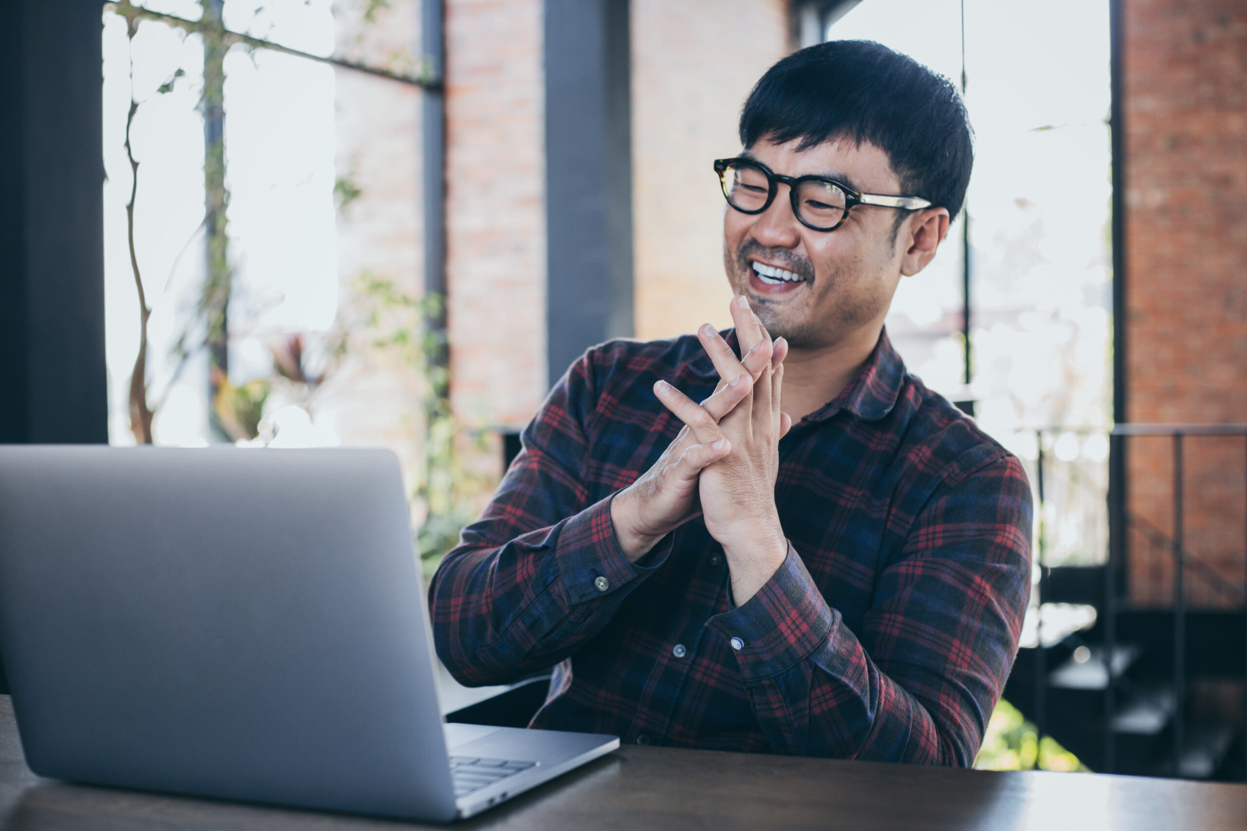 Asian man with glasses working on laptop during online interview, supporting Fluid Resourcing recruitment solutions and talent sourcing services