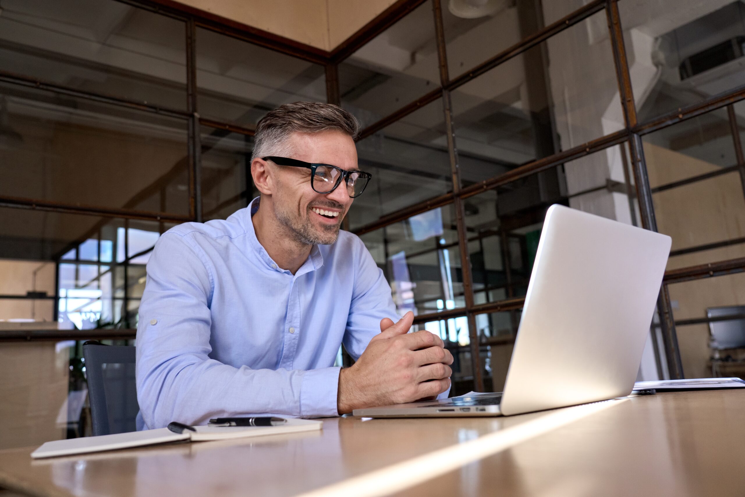 Smiling businessman in glasses using a laptop while communicating with a virtual assistant, reflecting Fluid Resourcing support solutions for businesses
