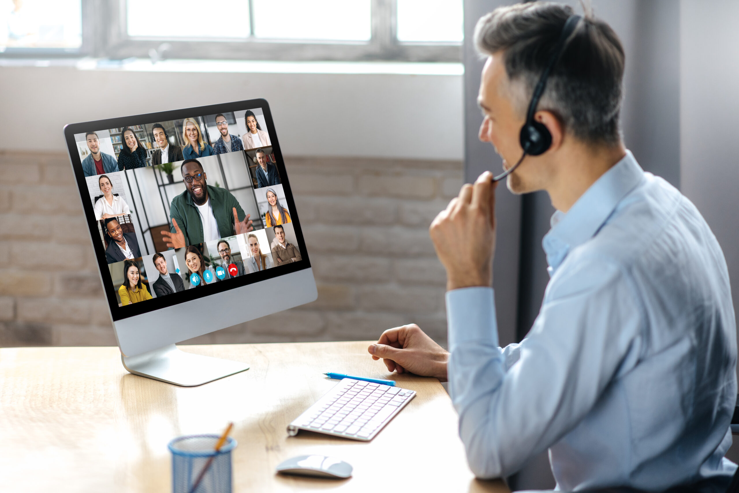 Man sitting at a desk using a computer in a virtual conference with multiple participants on screen for Fluid Resourcing services