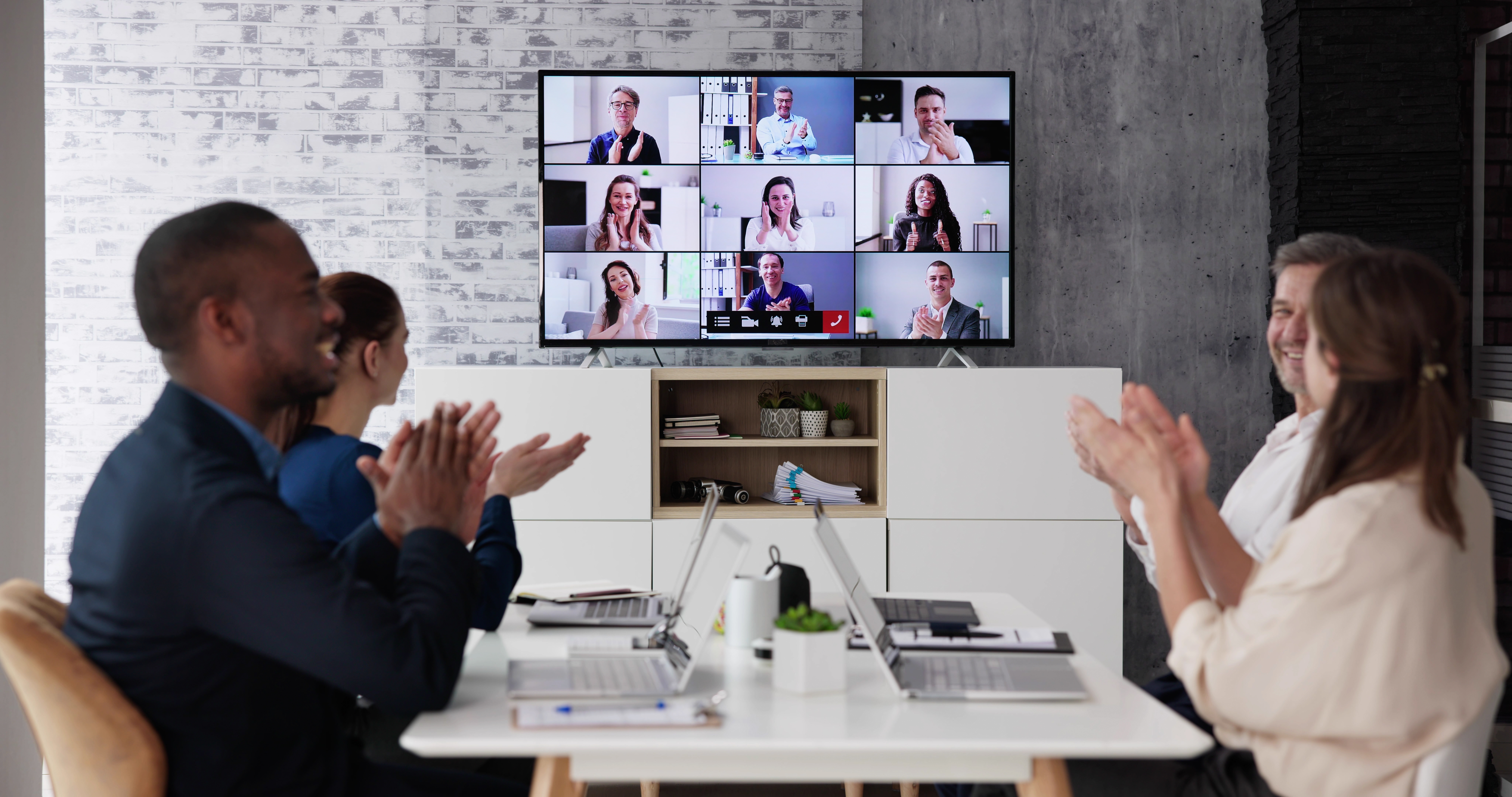 Joyful team in meeting room attending virtual conference via TV display, reflecting collaboration and Fluid Resourcing workplace engagement