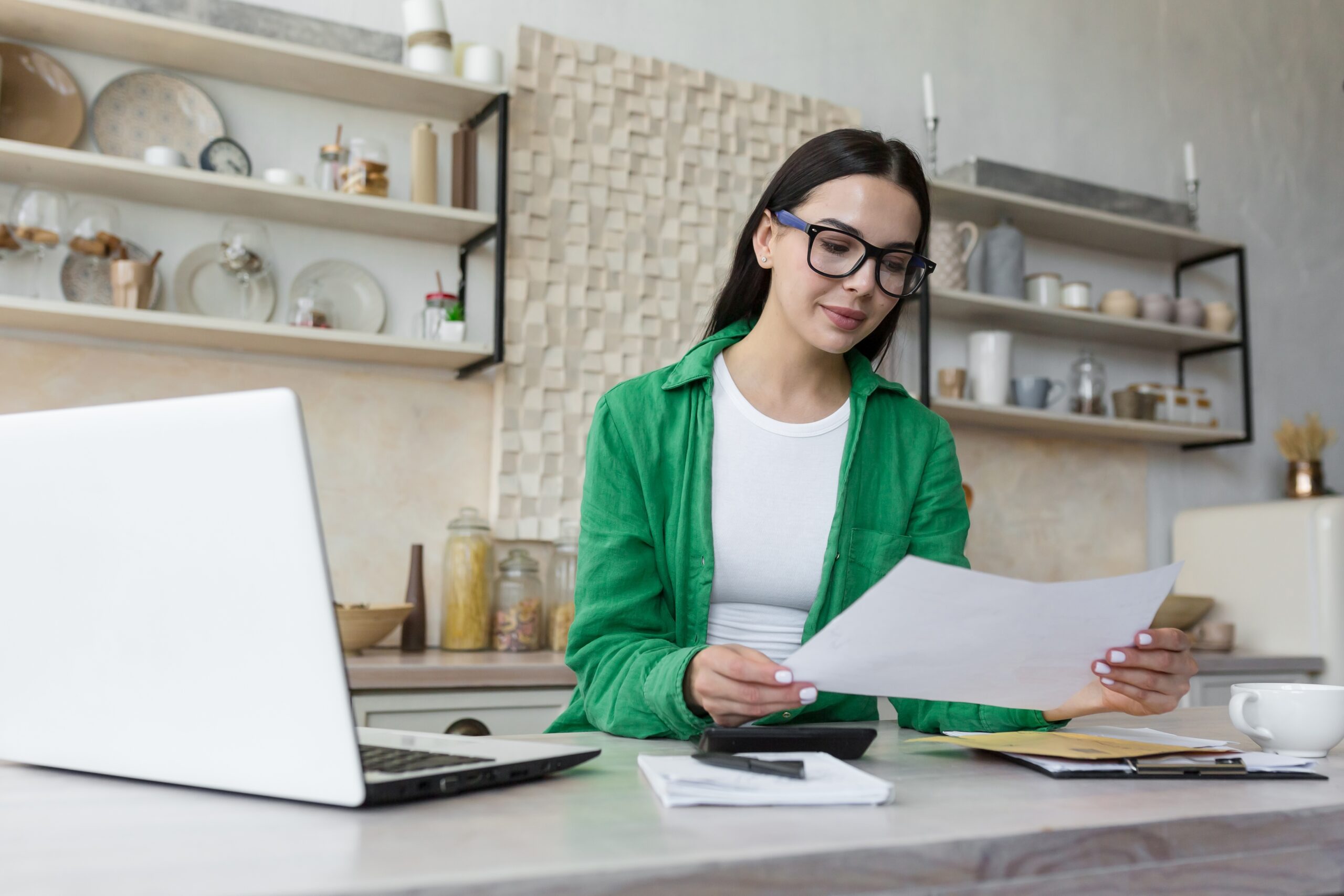 Woman wearing glasses working remotely with laptop and documents at a table, part of Fluid Resourcing professional services
